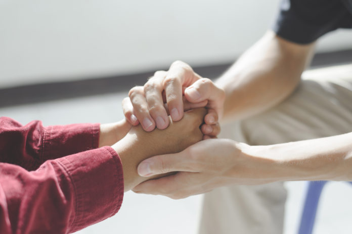 Close-up of man psychologist or psychiatrist sitting and holding hands palm of his woman patient for encouragement. PTSD Mental health concept, close up of two people holding hands