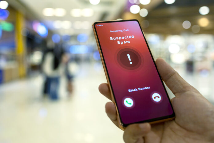 A man receiving an incoming suspected spam call on his phone. The network provider detect the scam and show warning sign to rejects the call. High angle view.