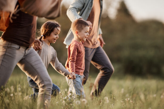 Happy siblings having fun while holding hands with their parents and running during spring day in nature.