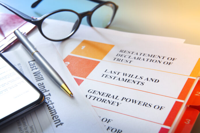 A ballpoint pen and a smart phone rest on top of living trust documents. A pair of eyeglasses sit out of focus in the background.